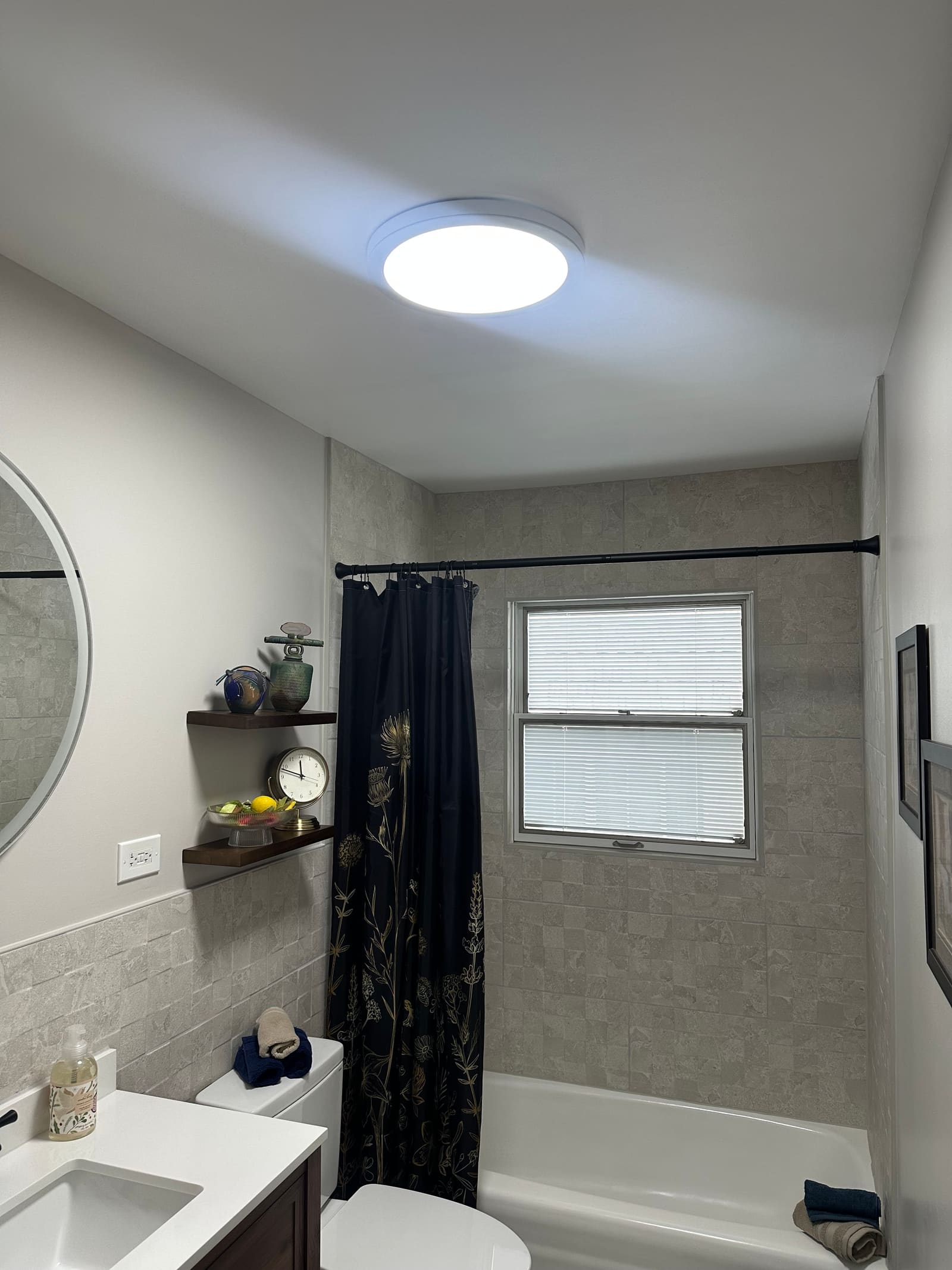 Wider view of the same bathroom showing new flush-mount ceiling light, floating walnut shelves, and tile wainscot.