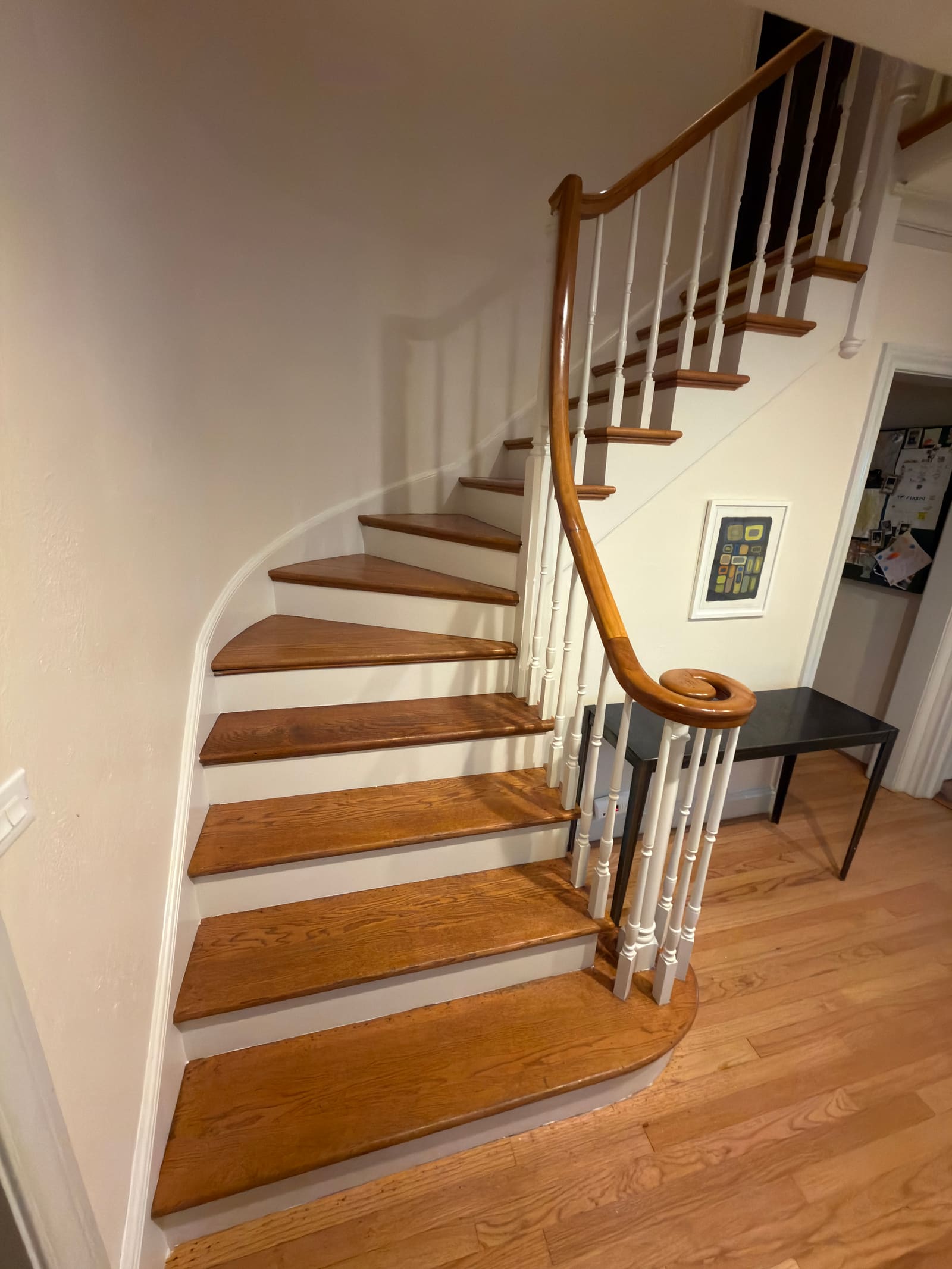 Curved oak staircase with white risers, white turned balusters, and an oak handrail curling into a volute at the bottom.