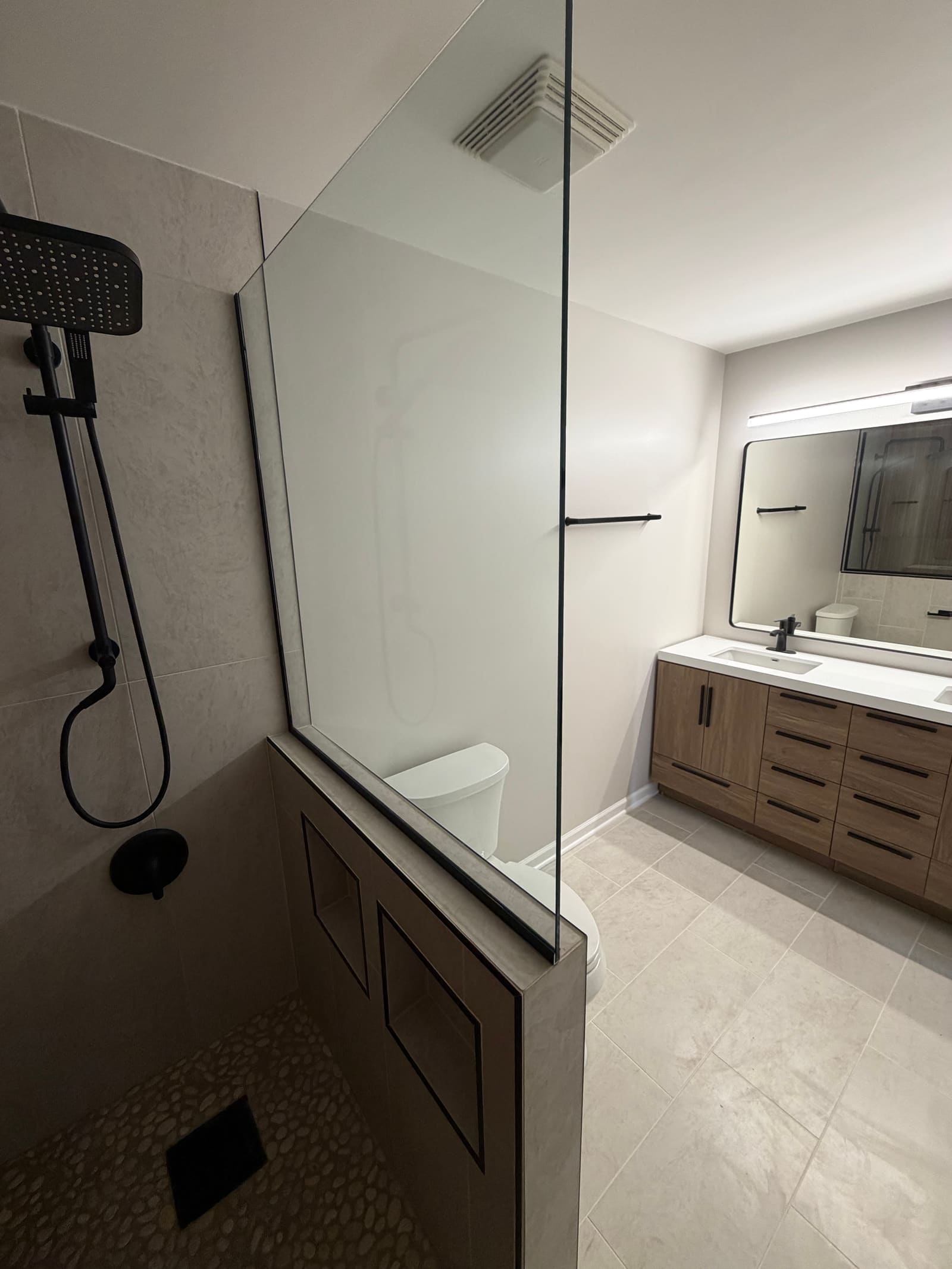 Bathroom with a glass-panelled walk-in shower on the left and a two-sink wood vanity with a lit mirror on the right.